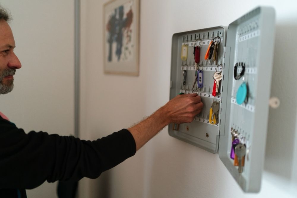Homme rangeant plusieurs clés étiquetées dans une armoire à clés murale